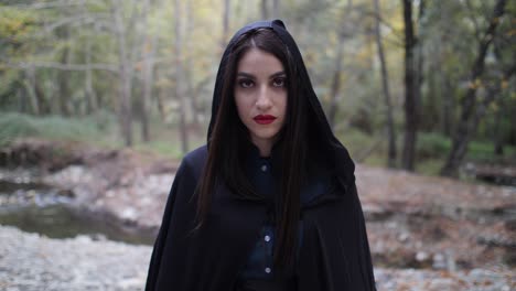 Portrait-of-a-mysterious-beautiful-woman-in-a-dark-cloak-as-she-looks-up-and-stares-deeply-into-the-camera-in-slow-motion