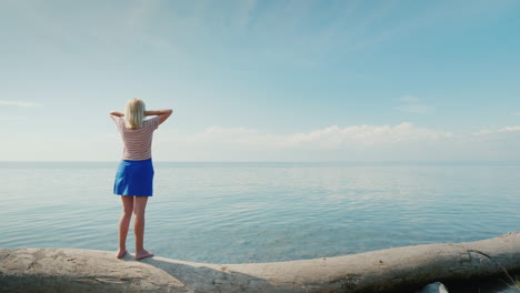 una joven parada en un tronco admira el hermoso paisaje donde el cielo se funde con el mar