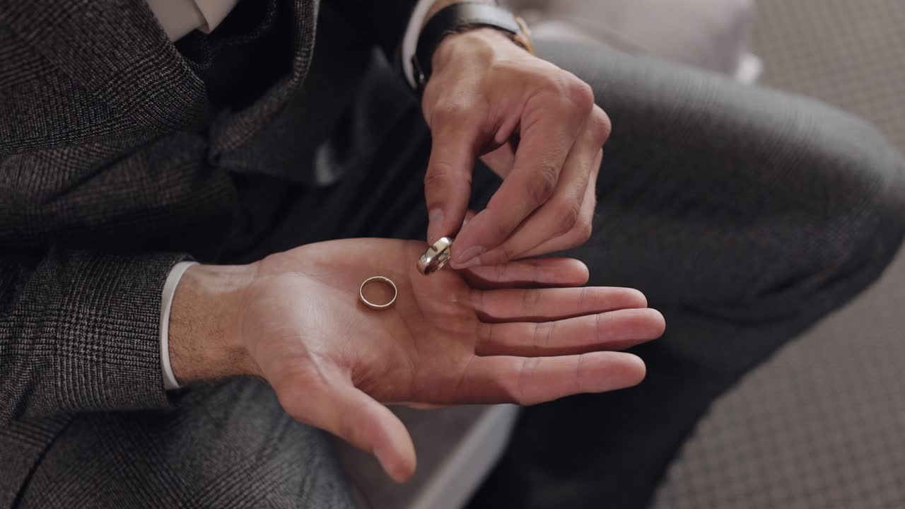 Groom in gray jacket holding wedding rings on palm of his hand, man touches the rings, slow motion