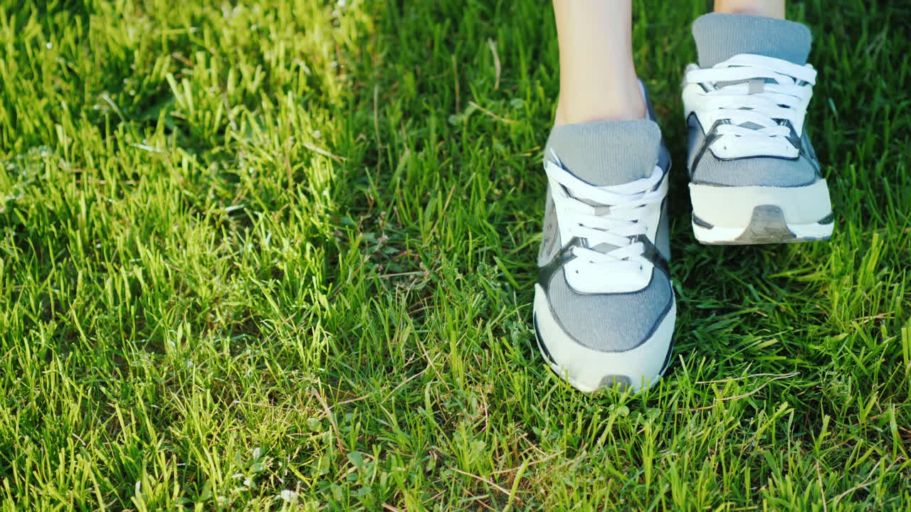 녹색 잔디 4k 슬로우 모션 비디오에서 흰색 운동화를 신은 여성 다리