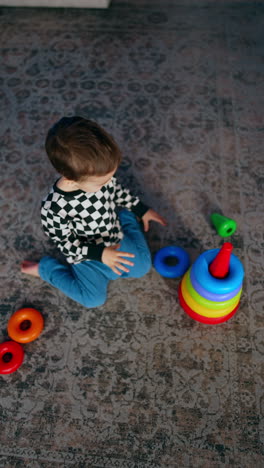 dark-haired baby boy sits on the carpet building a pyramid. top view on the child playing peacefully at home. vertical video.
