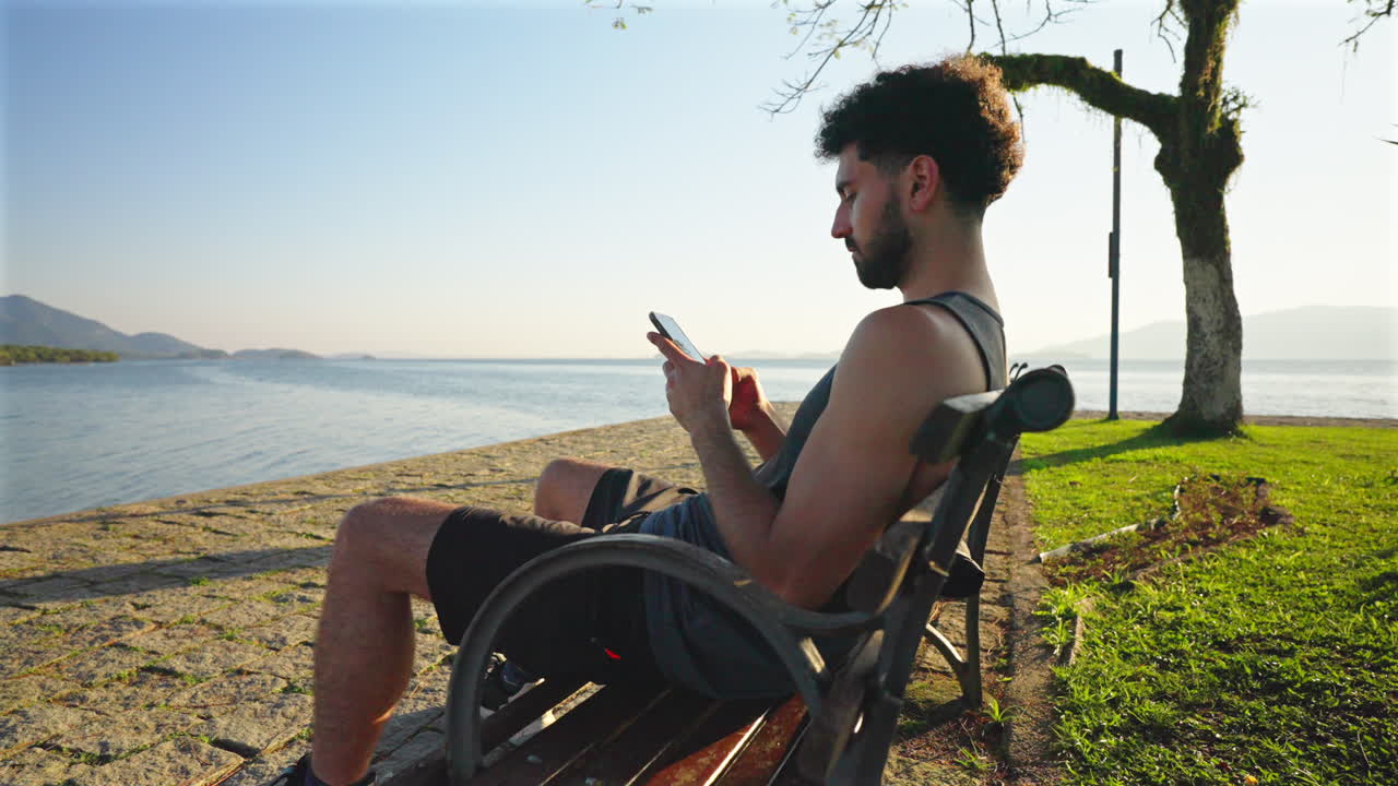 Man sitting by lake texting on his smartphone