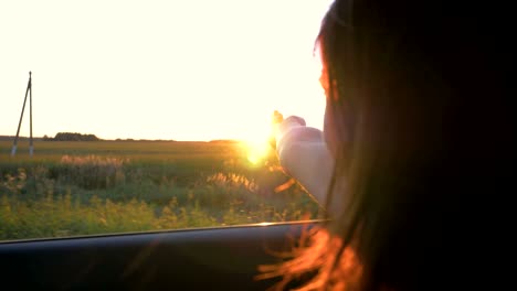 pretty young caucasian woman in car and hand playing in the air at sunset rays