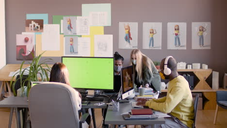 equipo multiétnico de diseñadores gráficos con máscaras faciales trabajando juntos en un estudio de animación