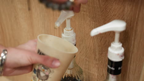 view of a hand wearing a bead bracelet and silver hand band holding a coffee cup while pumping coffee syrup.capturing the detailed process of adding syrup to the coffee cup