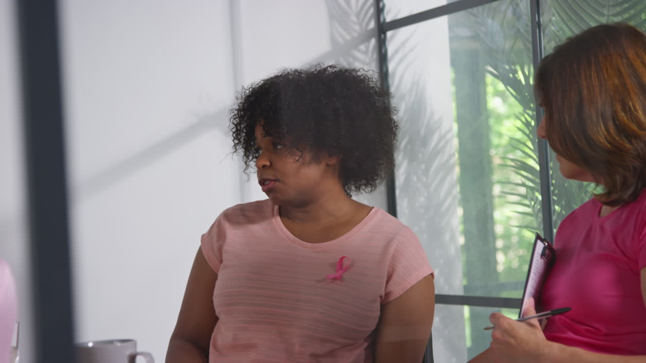 Group Of Women Wearing Pink Breast Cancer Awareness Ribbons Meeting And Talking At Therapy Support Group For Cancer Treatment Patients With Counsellor 1