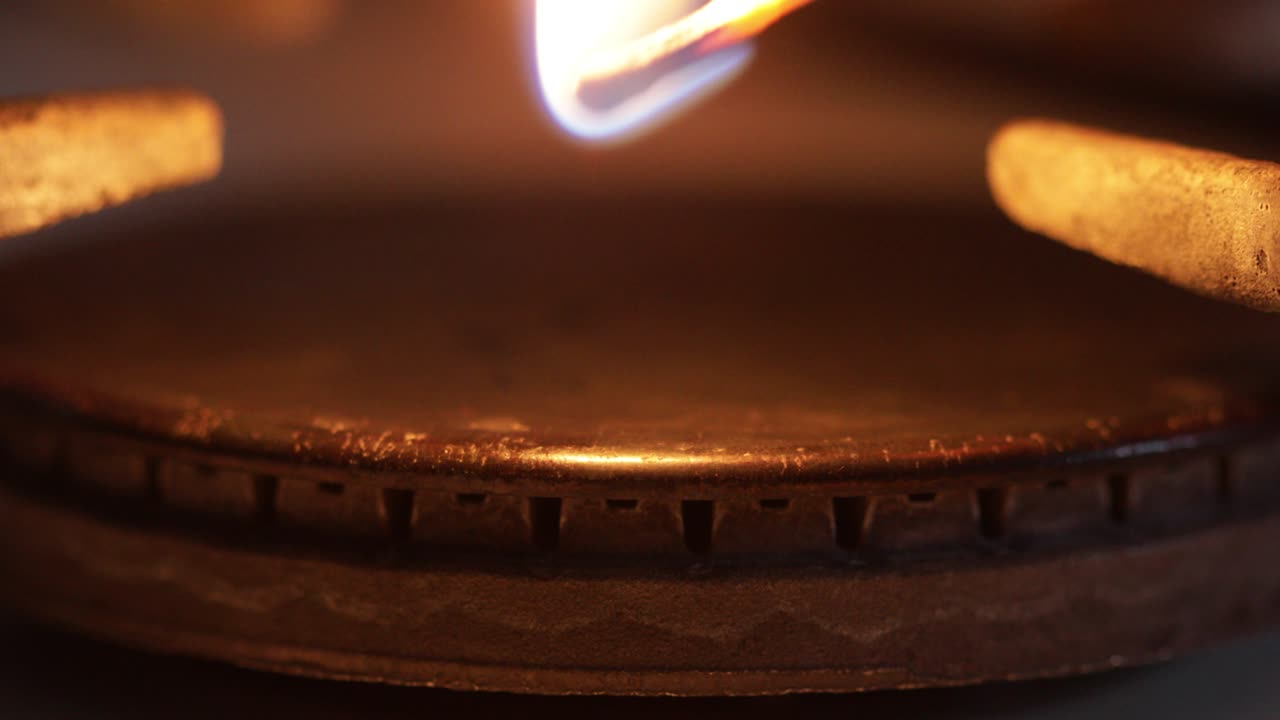 오래된 전통적인 가스 스토브를 비추는 불타는 매치를 가진 세부 사항.
