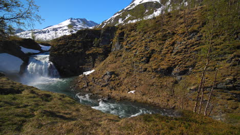 Static-view-of-a-waterfall-with-snowy-mountain-in-the-background,-on-a-sunny,-summer-day,-in-the-Lyngen-alps,-North-Norway