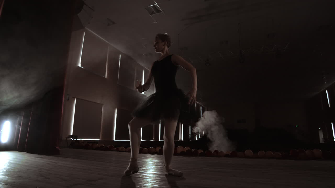 una bailarina bailando lentamente frente a las luces de los reflectores. varios reflectores muestran a una balerina bailando en un escenario oscuro en cámara lenta