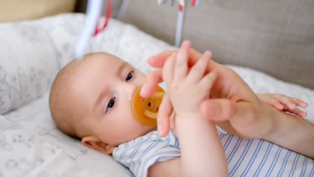 귀여운 작은 아기가 엄마의 손을 잡고 아기 침대에서 누워 있습니다.