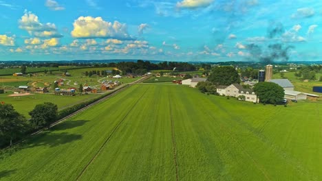 Eine-Luftaufnahme-Von-Amish-Ackerland-Mit-Einer-Einzigen-Eisenbahnstrecke-An-Einem-Sonnigen-Sommertag