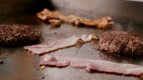 close up of uncooked bacon and cooked burger in hot griddle and smoke coming out