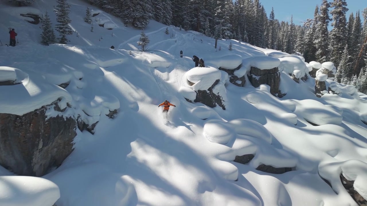 Snowboarder di sport estremi in azione fa snowboard su neve fresca profonda, cuscini di neve, scogliere, salti, curve aeree sulle Montagne Rocciose, Vail Pass, Colorado. Epic Ikon Breckenridge Copper Mountain, mattina d'inverno, seguito da drone.