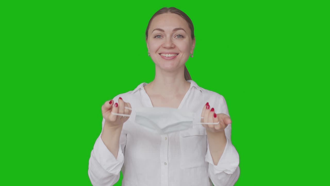 여성은 의학적 마스크를 벗고, 웃으며, 크로마키의 배경에서 행복하게 한숨을 쉬고, 여성은 의학적인 마스크를 제거합니다.