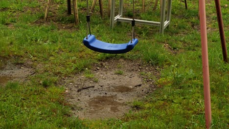 blue swing sways in rain on playground