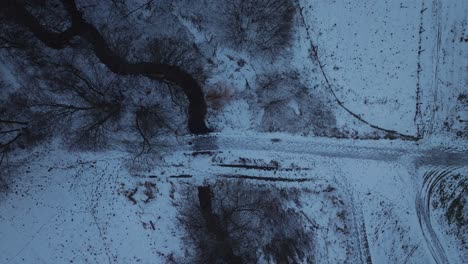 Top-down-shot-over-snow-covered-path-over-a-narrow-river-on-a-cold-winter-day