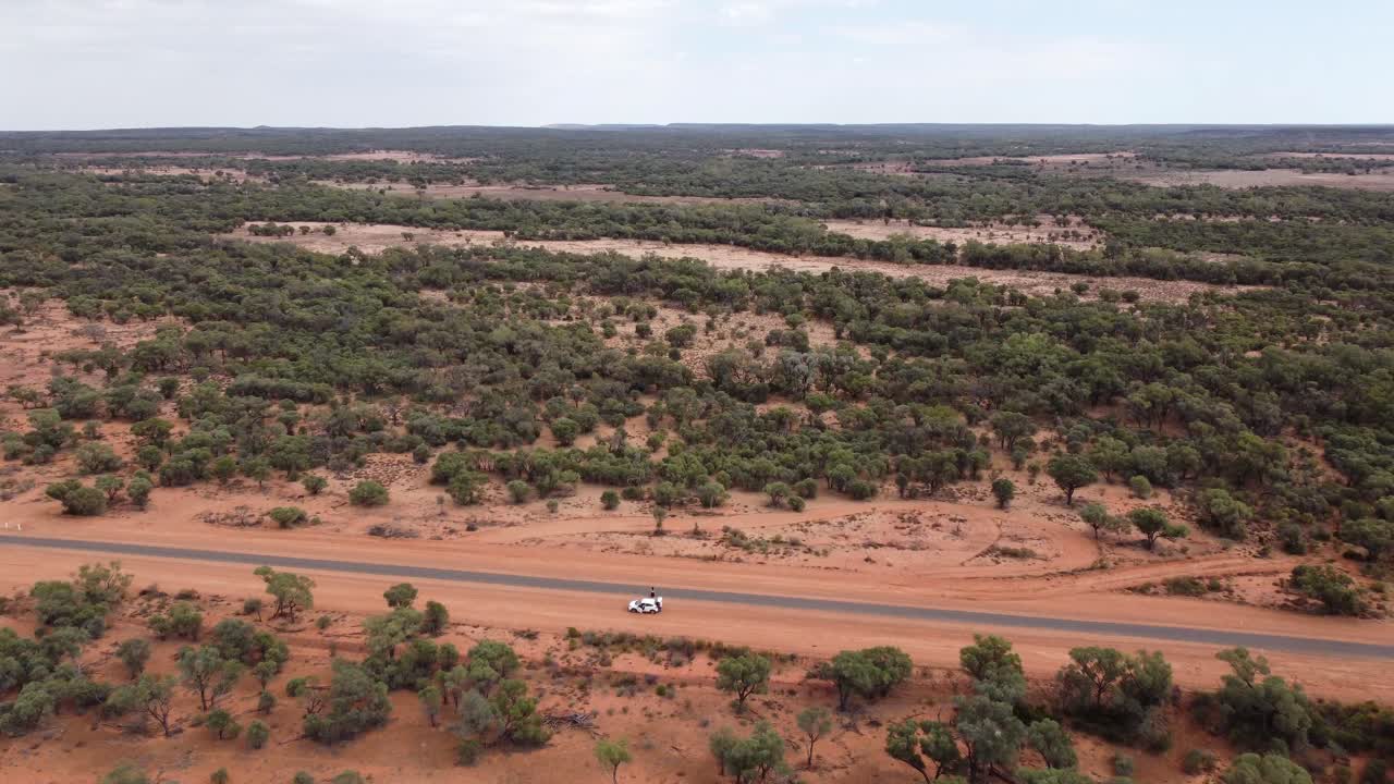 Avustralya Outback'inde park etmiş beyaz bir arabanın ve bir köy yolunun üzerinden bir hayvancılık mülküne doğru uçan drone.