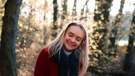 portret van een mooie jonge vrouw lachend in een rode jas te midden van de oranjebruine herfstbosbossen gevuld met fel warm zonlicht