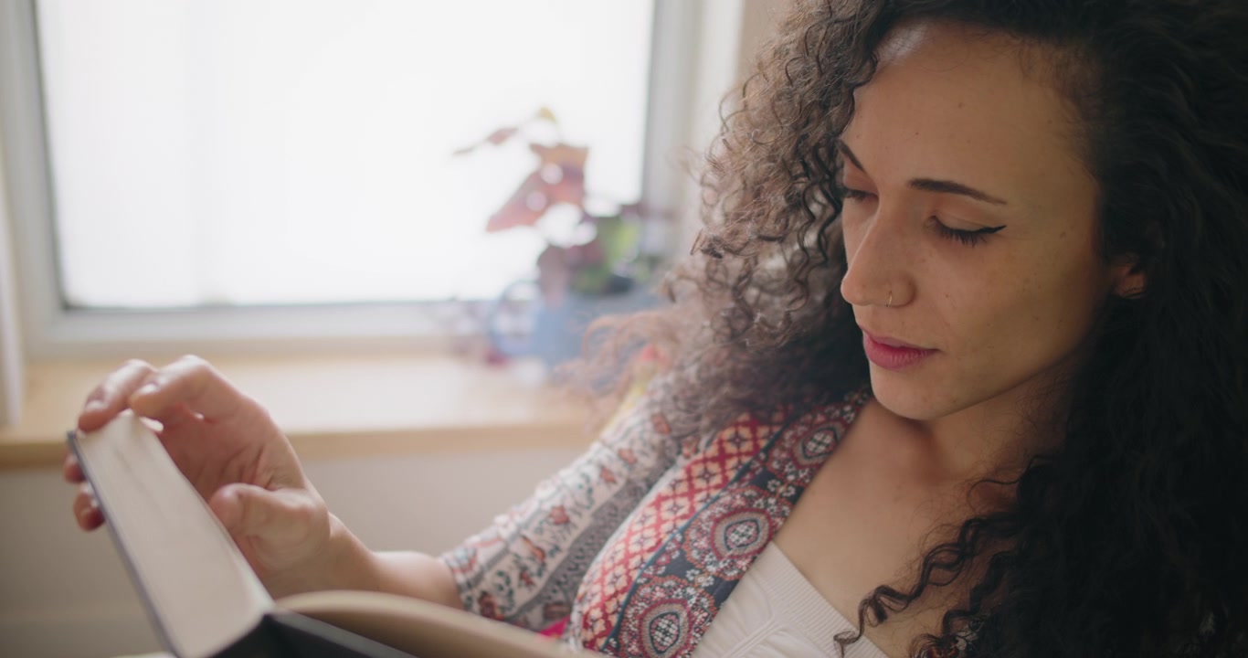 Giovane donna con i capelli ricci che legge un libro a casa