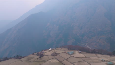 aerial shot of phortse village on everest base camp trail, dull and polluted skies, terrace farms, stupa, and surrounding himalayan hills in haze