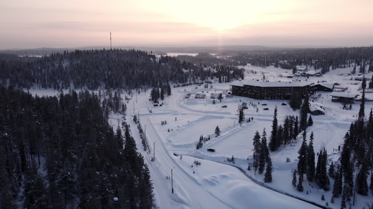 Dronebilde av Ruka skianlegg og by i snø i Lappland ved soloppgang.