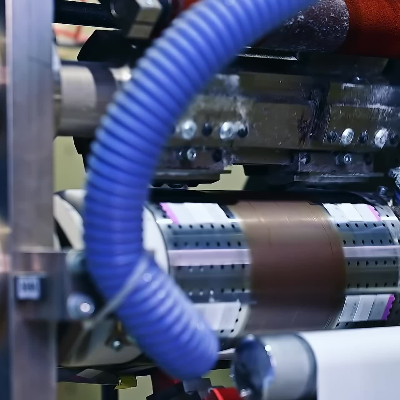 Enterprise for the production of diapers. Spinning shafts rotate and move the white layer between the gears of machine. Mechanism at work close up