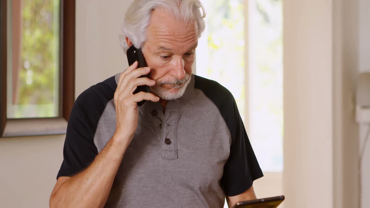 Senior man talking on mobile phone while using digital tablet 4k