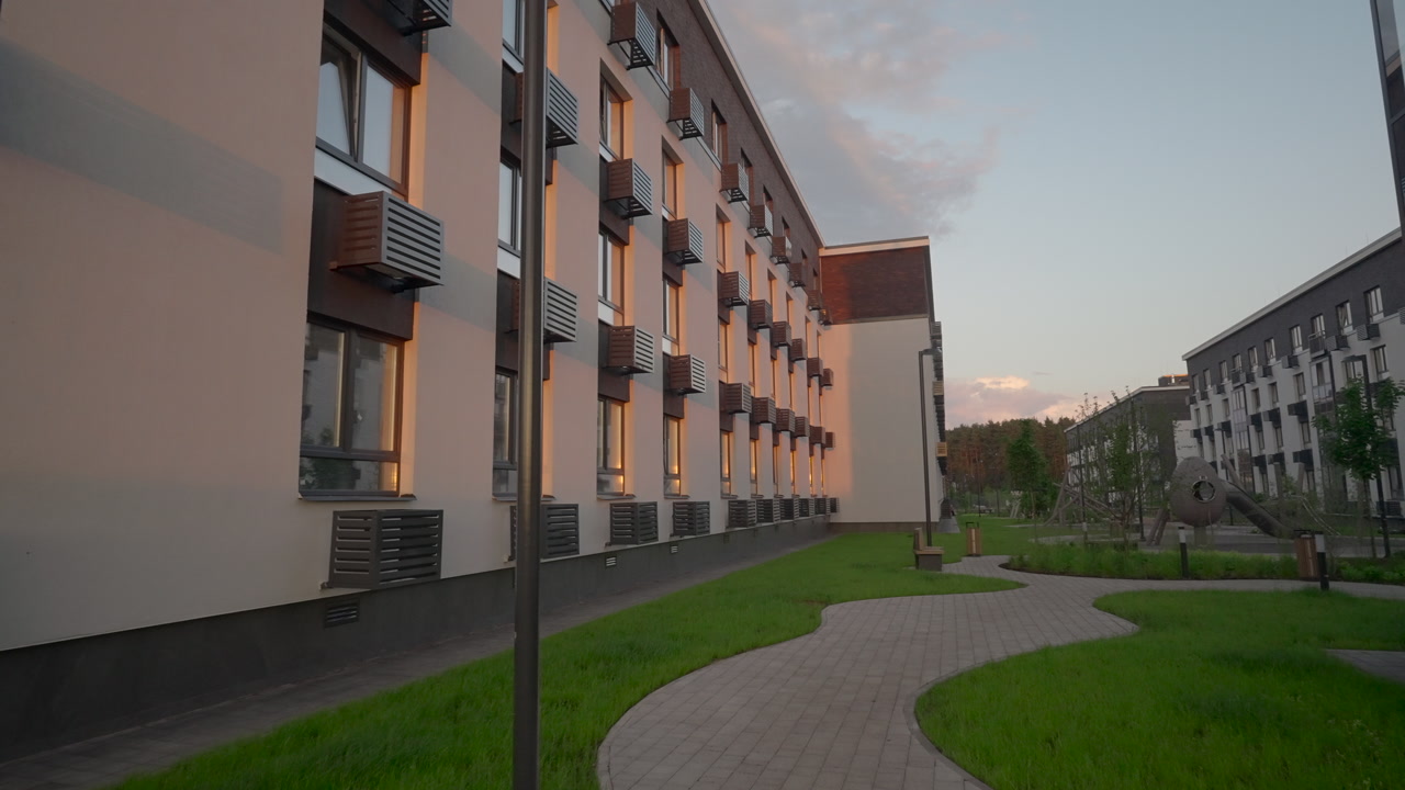 Winding Pathway Through Sunlit Apartment Courtyard, Warm Glow On Windows And Walls, Lamppost And Green Lawns
