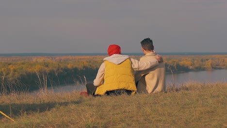 man sits near boyfriend and hugs on river bank edge slow