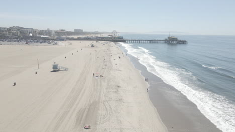 Blick-Aus-Der-Vogelperspektive-Auf-Den-Strand-Und-Den-Pier-Von-Santa-Monica,-Da-Viele-Draußen-Das-Schöne-Wetter-Genießen