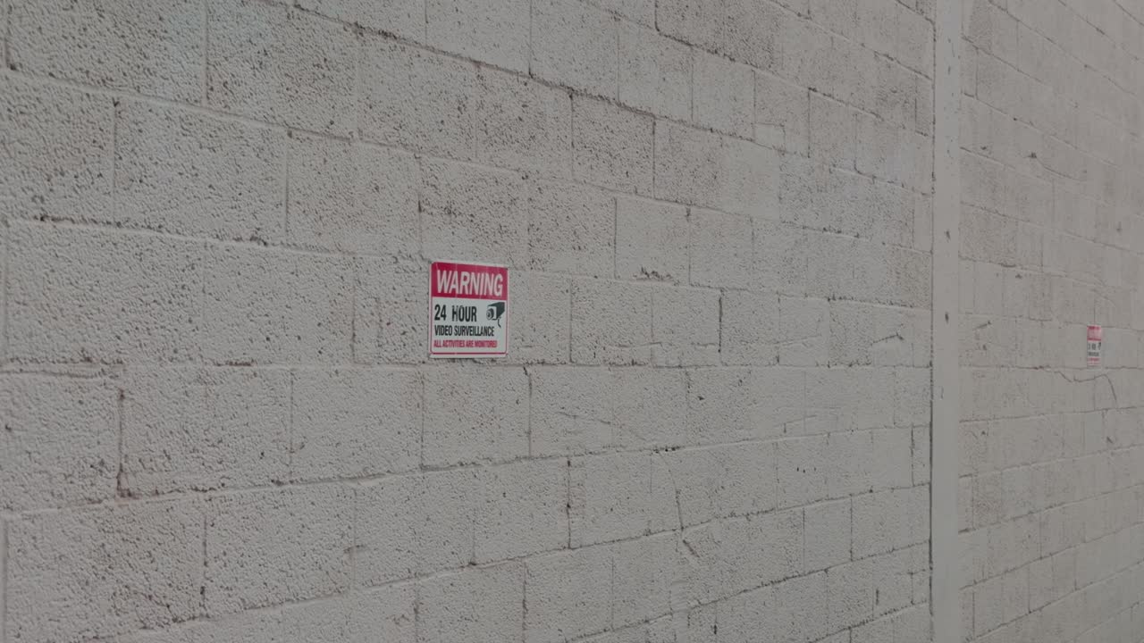 Waarschuwingsbord voor beveiliging gemonteerd op een ruwe witte betonblokmuur buiten