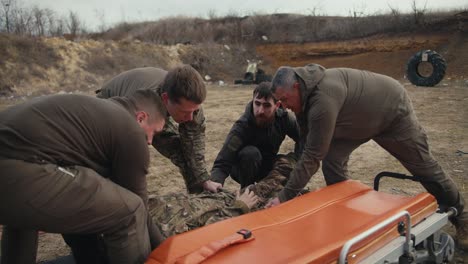 four confident men and a soldier in a green uniform shift a training doll of a male soldier in a camouflage uniform onto an ambulance worn during training in providing medical assistance on the battlefield