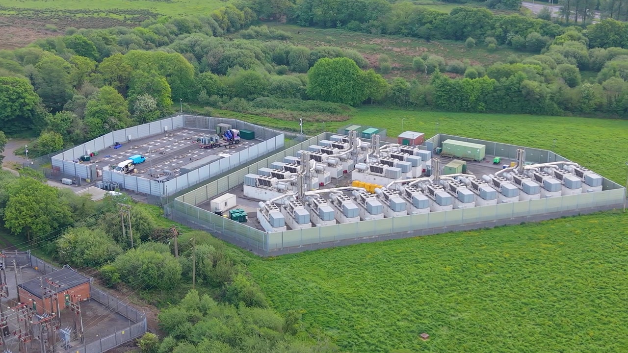 Slow Sideways Aerial of Modern Gas Peaking Plant with exhaust stacks, generators with BESS under construction for greater grid stability. Rapid-response electricity during peak demand in UK.
