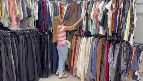young woman choosing blouse in clothing store young woman in casual clothes chooses elegant blouse in store