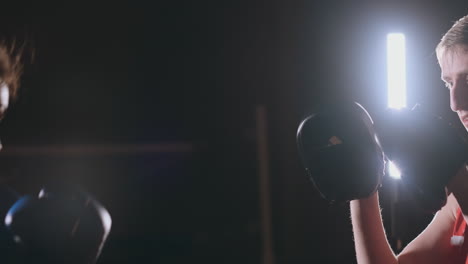 Medium-shot-of-beautiful-fitness-woman-boxer-treneruemsya-strike-speed-focus-mitts-with-a-coach-in-a-Boxing-club.-slow-motion