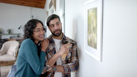 Feliz-Pareja-Birracial-Mirando-Pintura-En-La-Pared-De-Casa,-En-Cámara-Lenta