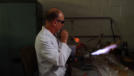 vista lateral de un trabajador caucásico soplando vidrio en una fábrica de vidrio 4k