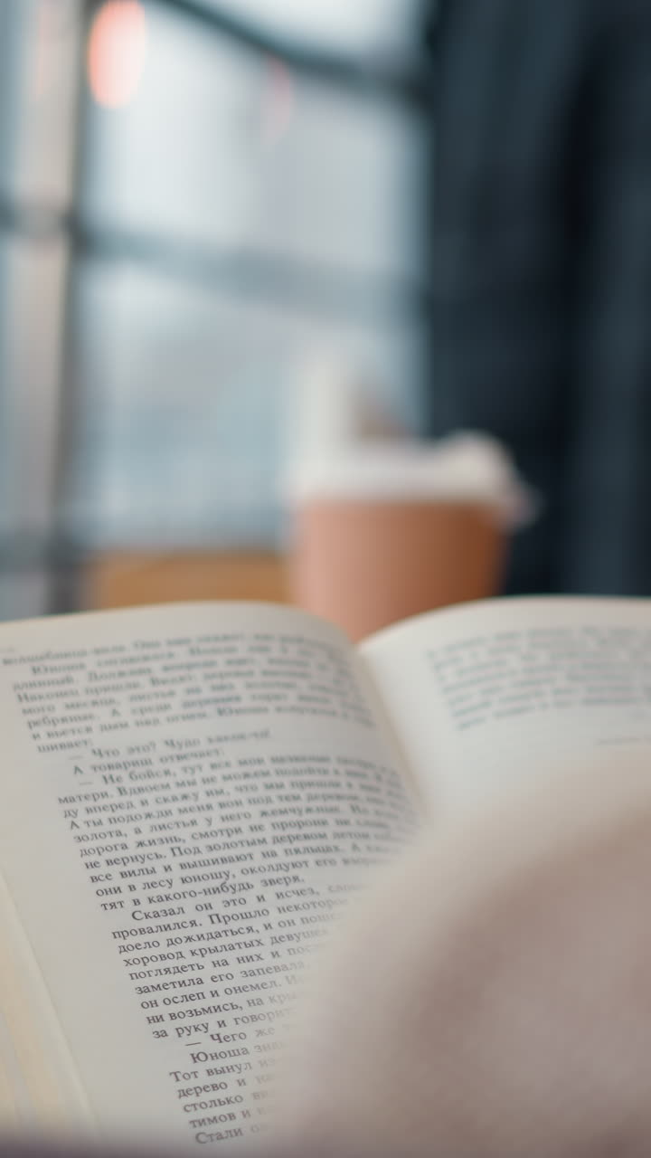 vista trasera de primer plano de una dama volviendo a una nueva página en un libro con una taza de té en la mesa en el frente, fondo borroso que muestra a personas fuera de foco en el centro comercial