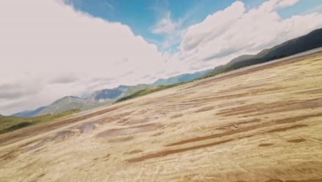 Low-flying-FPV-aerial-over-dried-up-expanse-of-Stave-Lake-showcasing-rugged-rocks-dust-laden-surfaces,-fallen-logs-tree-stumps-bright-sunny-day-wispy-clouds-sky-Beautiful-exciting-adventurous