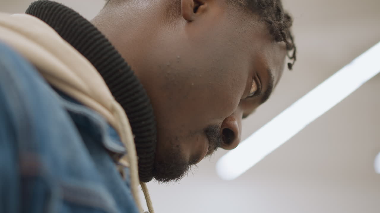 Close-up of man looking down, focused on reading or examining something, with soft ambient lighting and a neutral background, highlighting concentration and calm attention