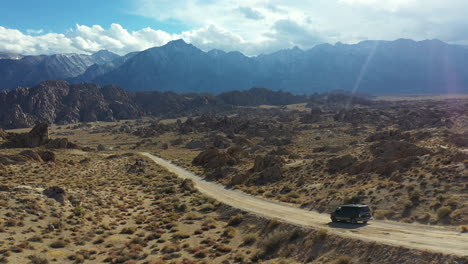 dark van on desert road, cinematic tracking aerial view of vehicle moving in dry landscape of alabama hills, california usa