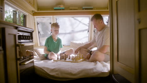 father and son playing chess sitting on the campervan bed