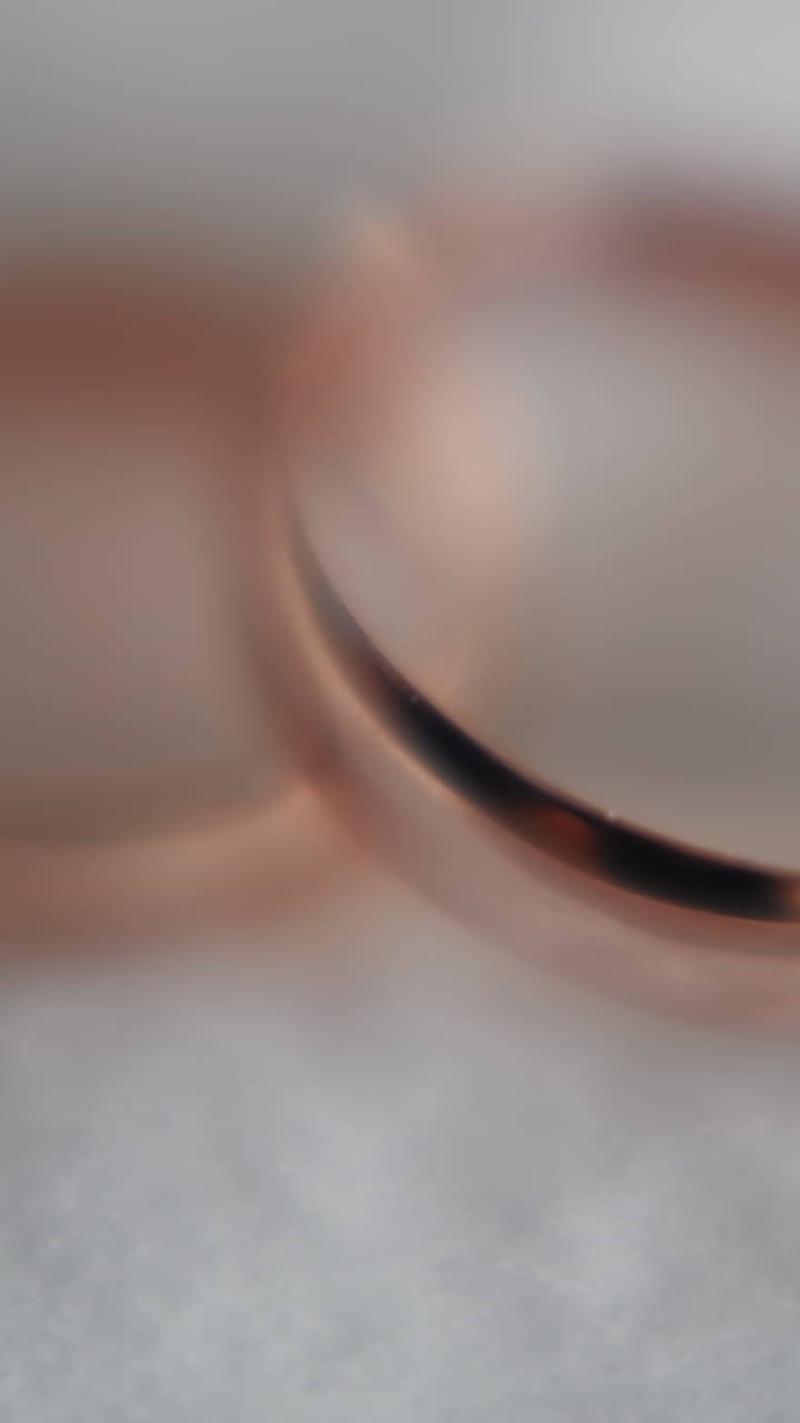 Gold wedding rings pair on soft white fabric extreme closeup. Glisten precious jewelry items for newlywed couple. Bridal ceremony accessory