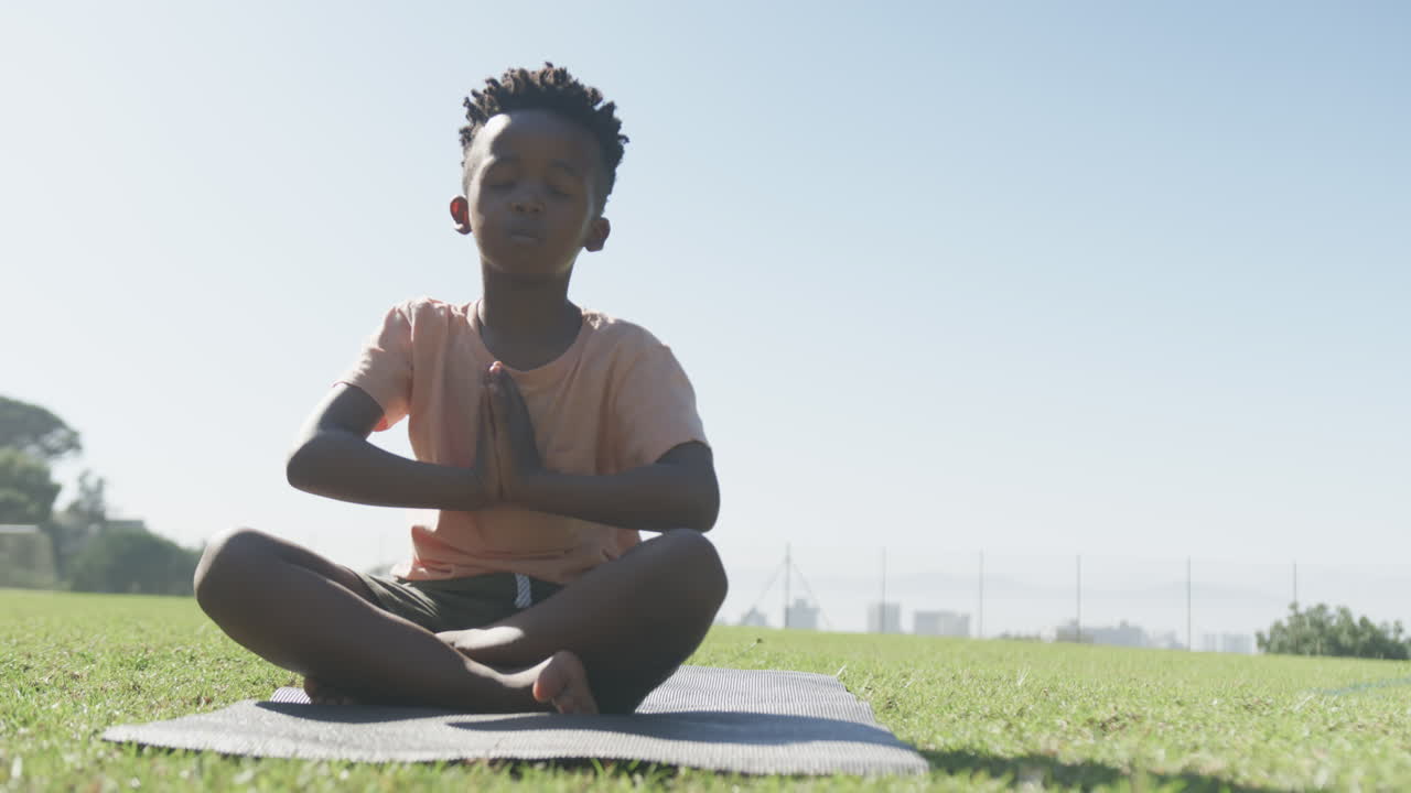 Meditating on yoga mat, boy practicing mindfulness outdoors in school setting, copy space