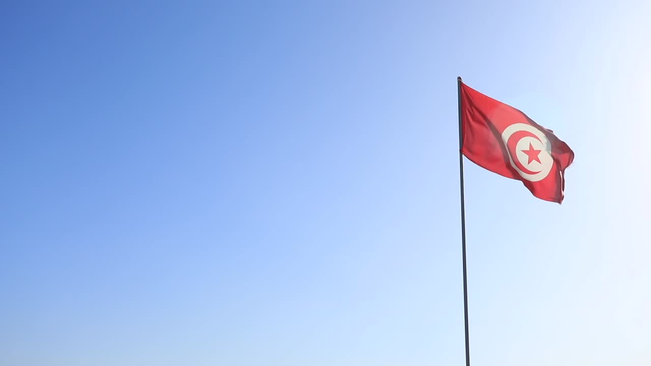 Berrak mavi bir gökyüzüne karşı dalgalanan Tunus bayrağı, ulusal gurur vurgusuyla.