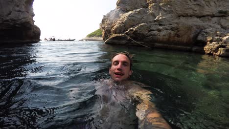 man swimming on back on surface of clear water in a secluded cove of hvar, croatia dives underwater