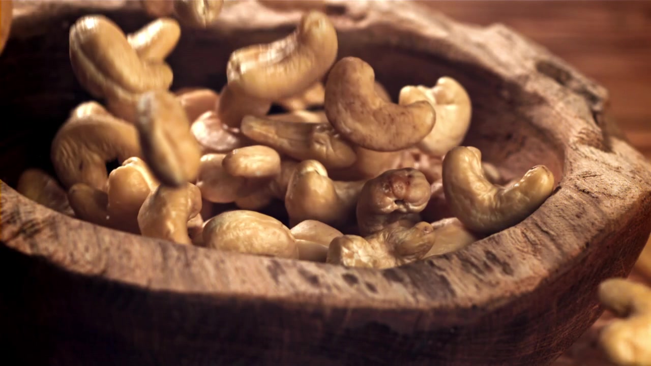 Cashewnøtter faller ned i en rustikk treskål i sakte film