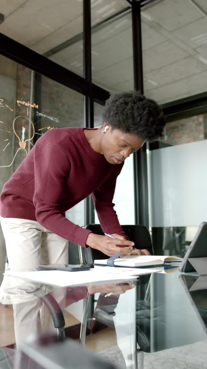 Vertical video of african american man using tablet and taking notes at home, slow motion