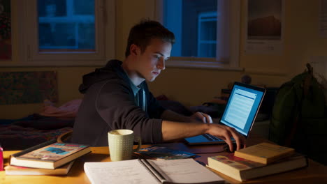 young man studying on a laptop at his desk at night