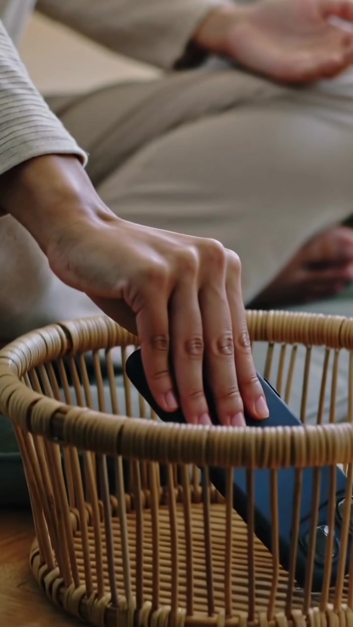 Vertikální video: Zvedá telefon, žena v béžovém topu jej vkládá do košíku ve studiu na cvičení.